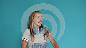 A little girl with big white teeth dancing on a blue background. Teen girl with bright, bright blue headphones, rejoices