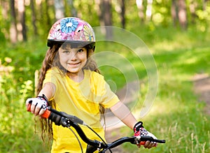 Little girl on bike in forest looking at camera and smiling