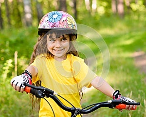 Little girl on bike in forest looking at camera and smiling