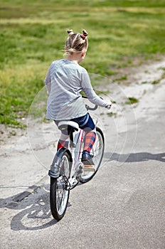 Little girl biking on sunny summer day in city park.