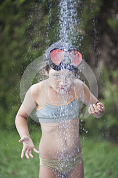 Little girl in a bikini in the jet of water in the shower