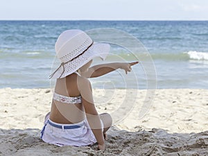 Little girl in a bikini looks at the sea and points his finger to the side