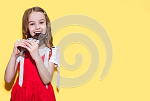 Little girl bites a bar of chocolate on a yellow background