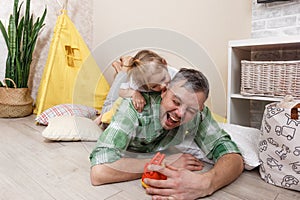 A little girl bites her father& x27;s ear while playing together. A loving father
