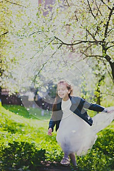 Little girl in black jacket and white dress dancing in the spring cherry garden