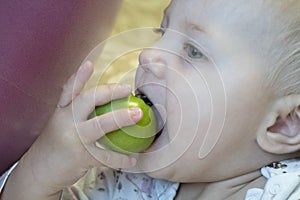A little girl with blond hair with a green tomato in her hand