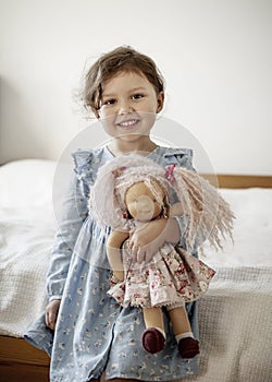 Little girl with blond hair holding her doll and smiling