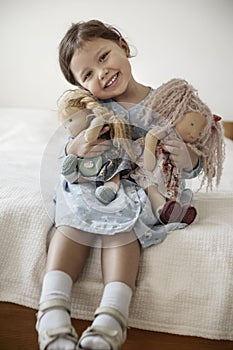 Little girl with blond hair holding her dolls and smiling
