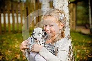 Little girl with blond hair plays with pup on a garden background.Little girl holds a puppy on her arms.Cute little girl