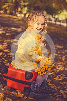 Little girl with blond hair and suitcase in autumn background