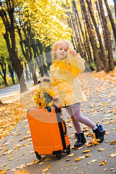 Little girl with blond hair and suitcase in autumn background