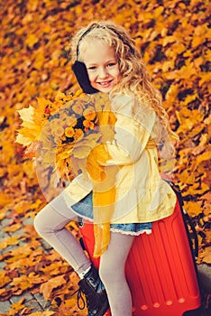 Little girl with blond hair and suitcase in autumn background