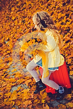 Little girl with blond hair and suitcase in autumn background