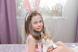 A little girl with blonde hair holds a red cat in her hands