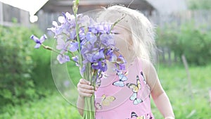 Little girl blonde sniffs a bouquet of blue irises.
