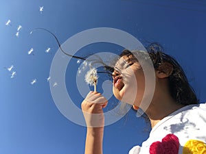 A little girl blowing dandelion seeds.