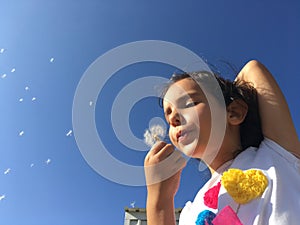 A little girl blowing dandelion seeds.