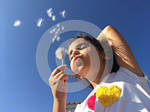 A little girl blowing dandelion seeds.