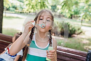 Little girl blowing soap bubbles in summer park