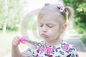 A little girl blowing soap bubbles in summer park