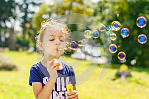 A little girl blowing soap bubbles in summer park.