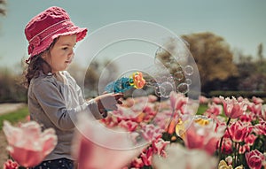 Little girl blowing soap bubbles in summer park and blooming tulips