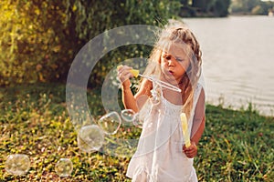 Little girl blowing soap bubbles in summer park. Child having fun