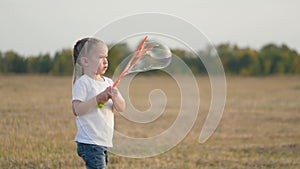 A little girl blows big bubbles at sunset. Childhood of a small child. Kid game in the park