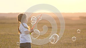 A little girl blows big bubbles at sunset. Childhood of a small child. Kid game in the park