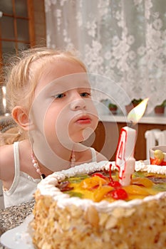 The little girl blows on a candle on a cake