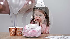 Little girl blows out candles on a birthday cake at home against a backdrop of balloons. Child's birthday.