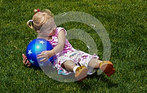 Little Girl with Blue Ball Rolling in Grass