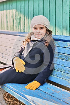 little girl in a blue coat on a park bench in autumn