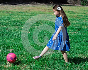 Little Girl in Blue Dress kicking soccer ball on Green Grass