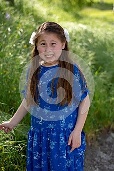 Little Girl in Blue Dress making funny and crazy face in front of green field