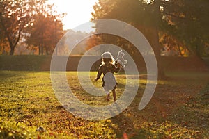 A little girl in a blue dress with a plush hare in her hand runs across the grass on a sunny autumn day.