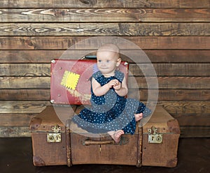 The little girl in blue dress sits on big suitcase.