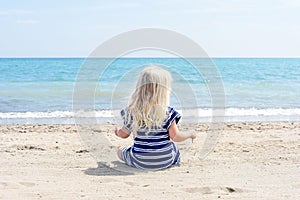 Little girl in blue dress sitting on the beach enjoying a beautiful day