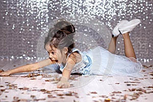 Little girl in blue dress sitting on the floor with confetti