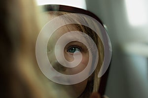 Little girl with blue eyes looking in the mirror. Cute serious curious child admires herself in reflection. Kid portrait