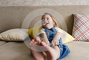 a little girl in a blue jumpsuit lies at home on the sofa among the colorful pillows and smiles cheerfully