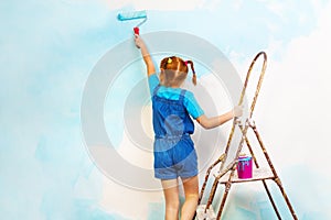 Little girl in blue paints the wall on a ladder