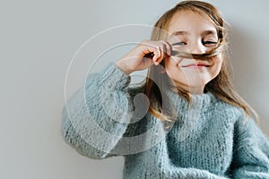 Little girl in a blue sweater playing with her hair, making fake mustache