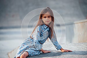 Little girl in blue wear posing for a camera in the city when leaning on the ramp