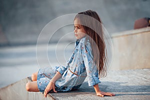 Little girl in blue wear posing for a camera in the city when leaning on the ramp