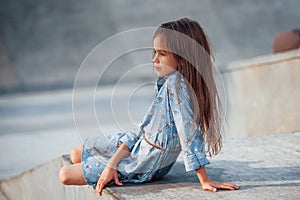 Little girl in blue wear posing for a camera in the city when leaning on the ramp