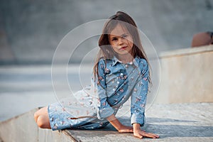 Little girl in blue wear posing for a camera in the city when leaning on the ramp