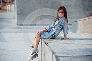 Little girl in blue wear posing for a camera in the city when leaning on the ramp