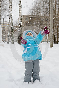 Little girl in a blue winter jacket plays with snow