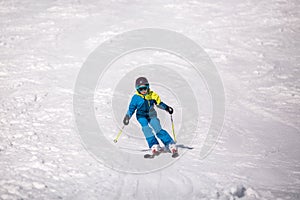 Little girl in blue and yellow ski costume skiing in downhill slope. Winter sport recreational activity